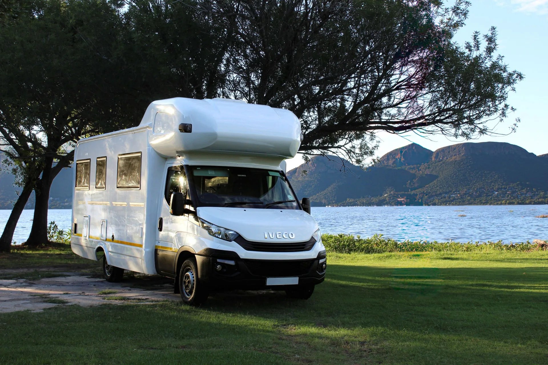 A motorhome parked beside a quiet lake and mountain landscape