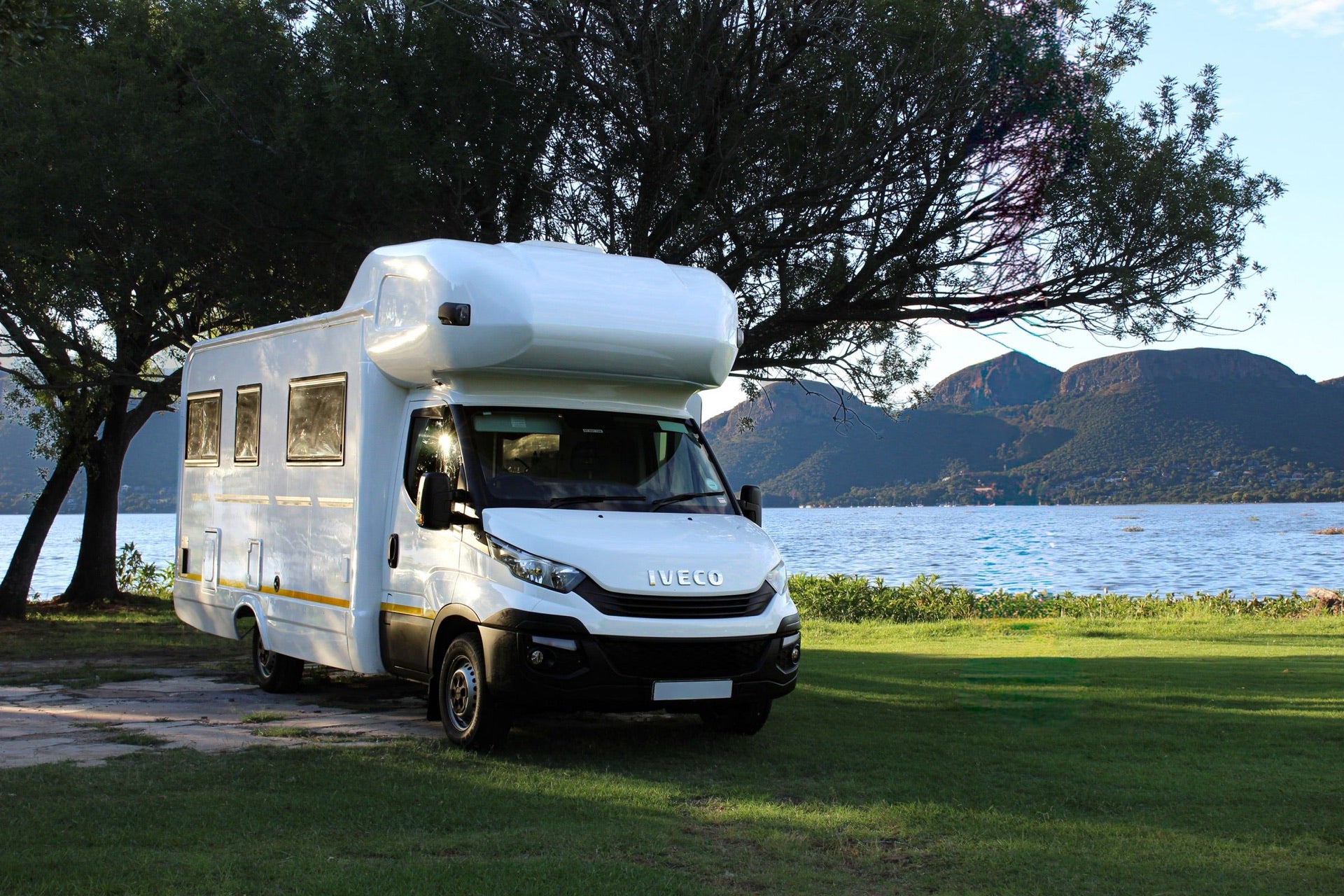 A motorhome parked beside a quiet lake and mountain landscape